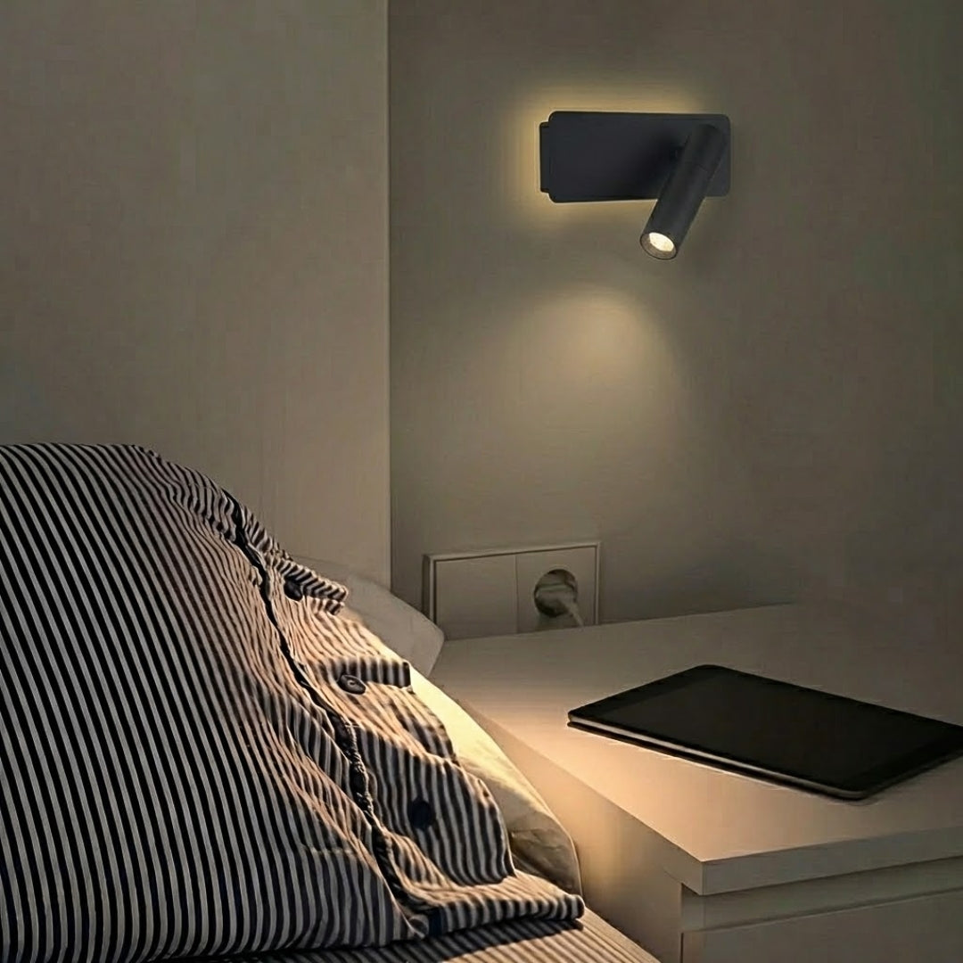 Czarna lampa ścienna skierowana na łóżko na białej ścianie.