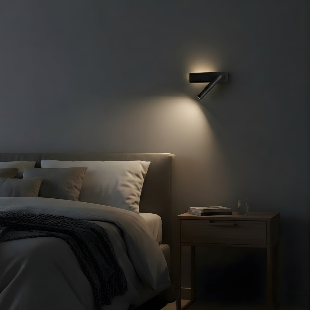 Czarna lampa ścienna skierowana na łóżko na szarej ścianie.