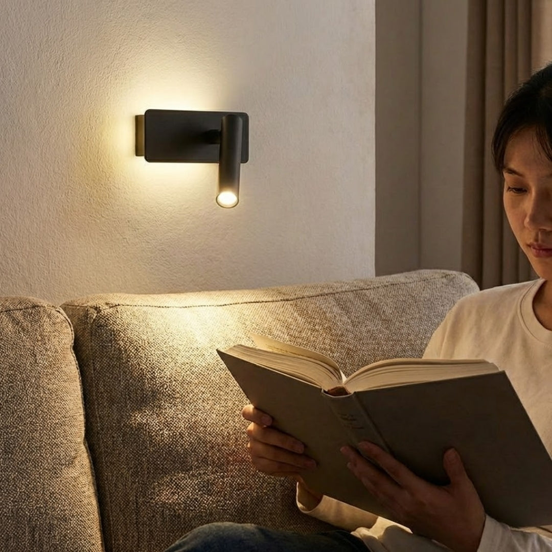 Kobieta czytająca na kanapie przy włączonej czarnej lampie ściennej skierowanej na książkę.